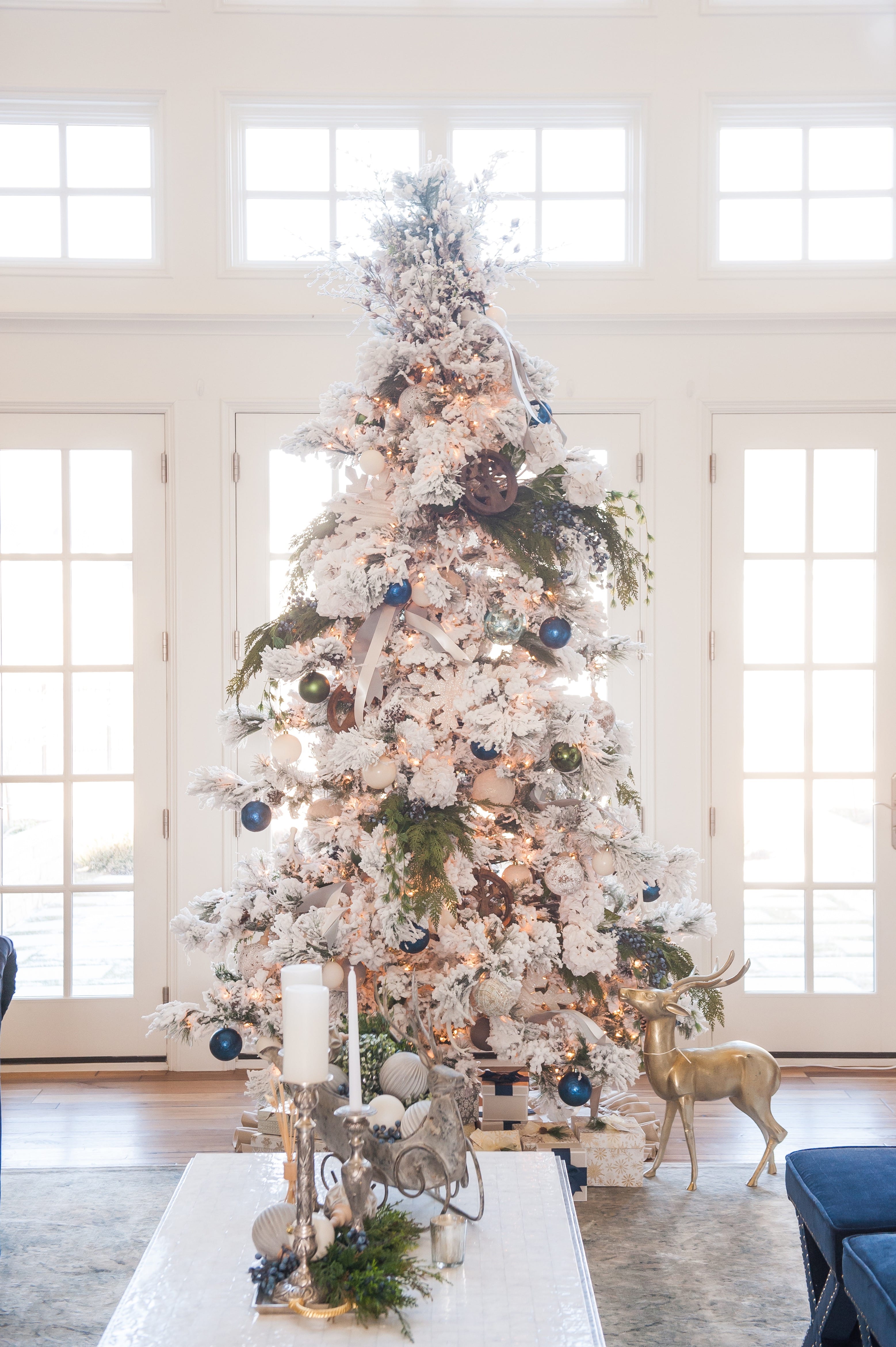 Christmas tree flocked long needle pine christmas tree flocked tree blue decor blue christmas ornaments trimming the tree shades of blue on white blue and cream flocked long needle pine artificial tree blue white ivory cream silver ornaments plaid ribbon