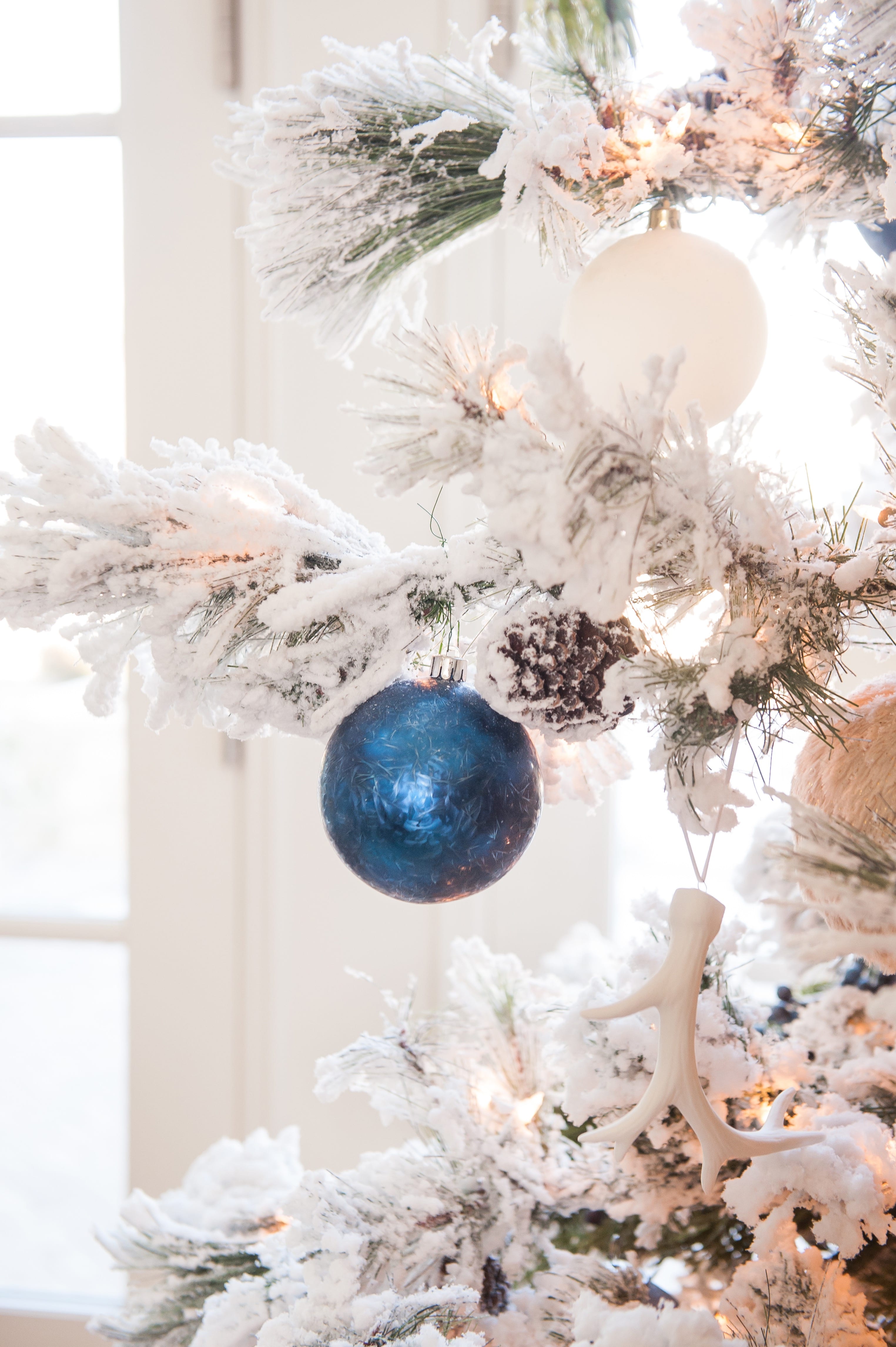 Christmas tree flocked long needle pine christmas tree flocked tree blue decor blue christmas ornaments trimming the tree shades of blue on white blue and cream flocked long needle pine artificial tree blue white ivory cream silver ornaments plaid ribbon