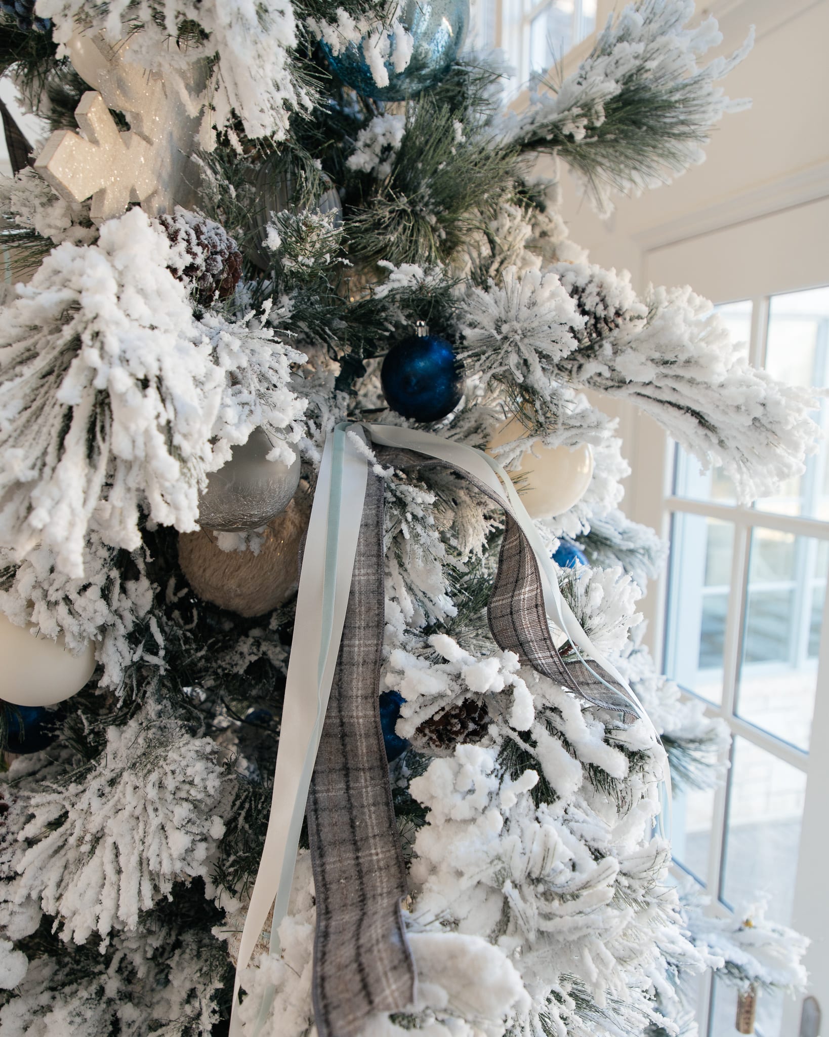 Christmas tree flocked long needle pine christmas tree flocked tree blue decor blue christmas ornaments trimming the tree shades of blue on white blue and cream flocked long needle pine artificial tree blue white ivory cream silver ornaments plaid ribbon