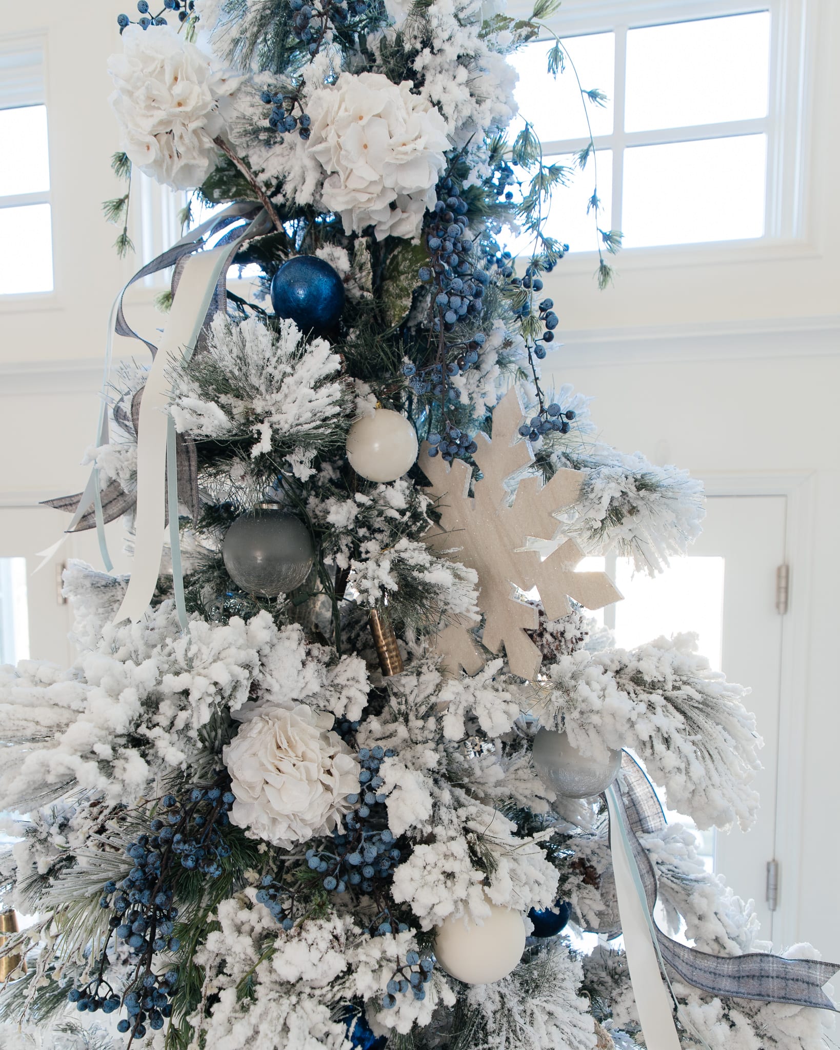 Christmas tree flocked long needle pine christmas tree flocked tree blue decor blue christmas ornaments trimming the tree shades of blue on white blue and cream flocked long needle pine artificial tree blue white ivory cream silver ornaments plaid ribbon